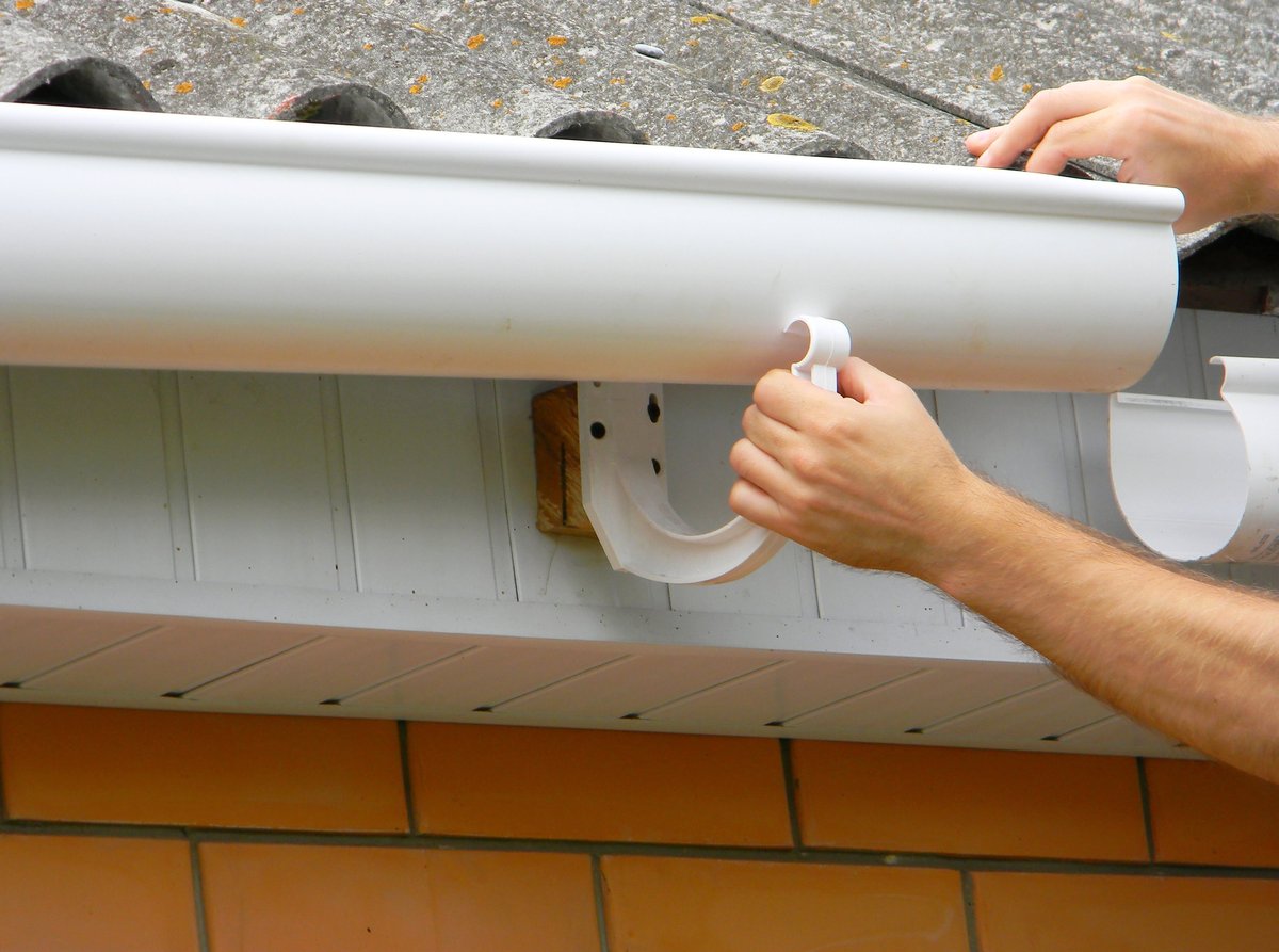 Contractor installing plastic roof gutter and rain guttering on a house by hand