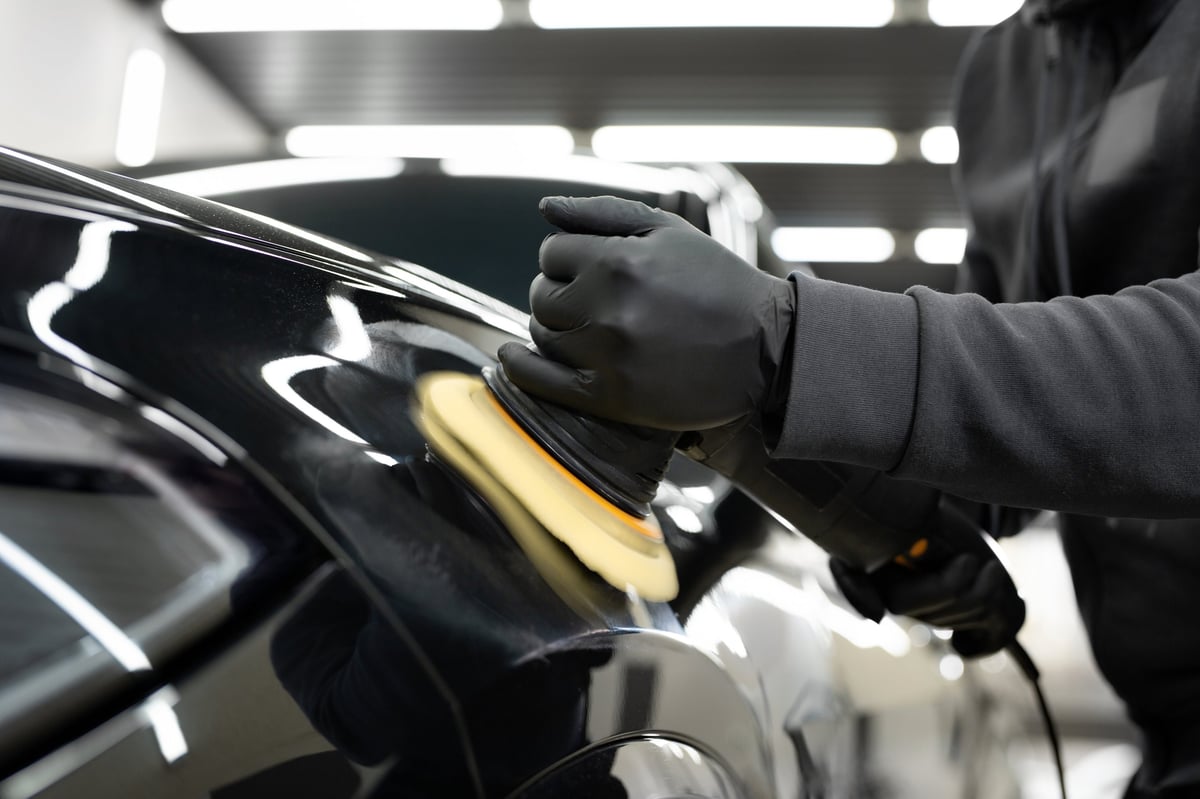 Professional car detailer polishing a vehicle with an orbital polisher in a detailing studio