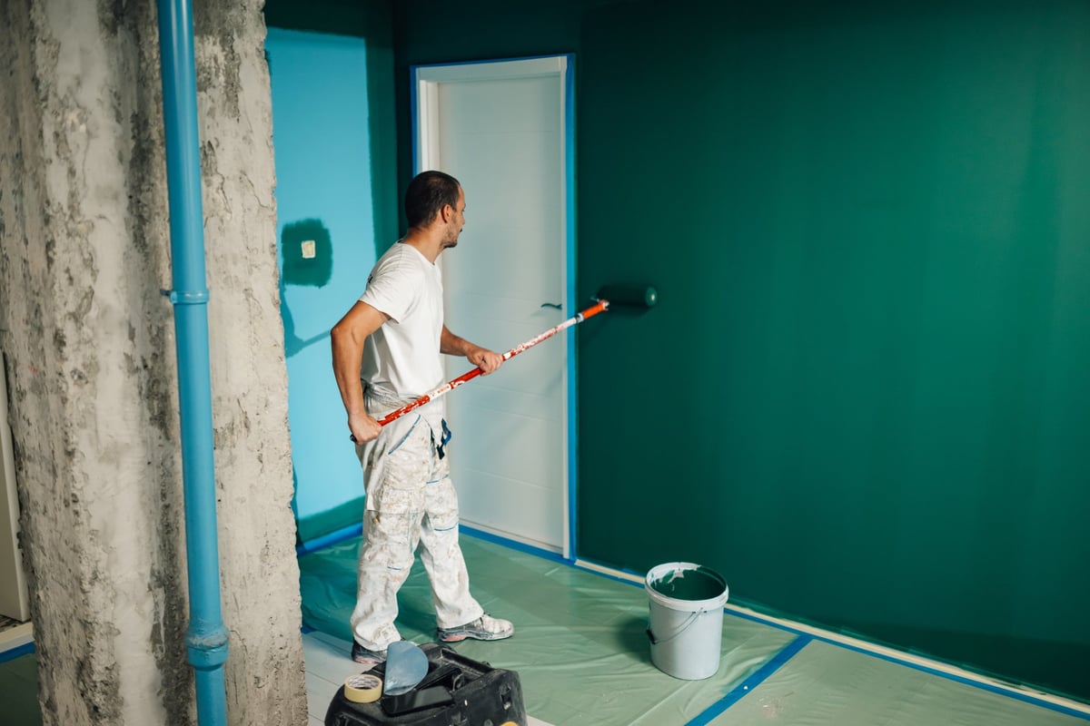 Professional painter using a paint roller applying green paint on a wall during a home renovation
