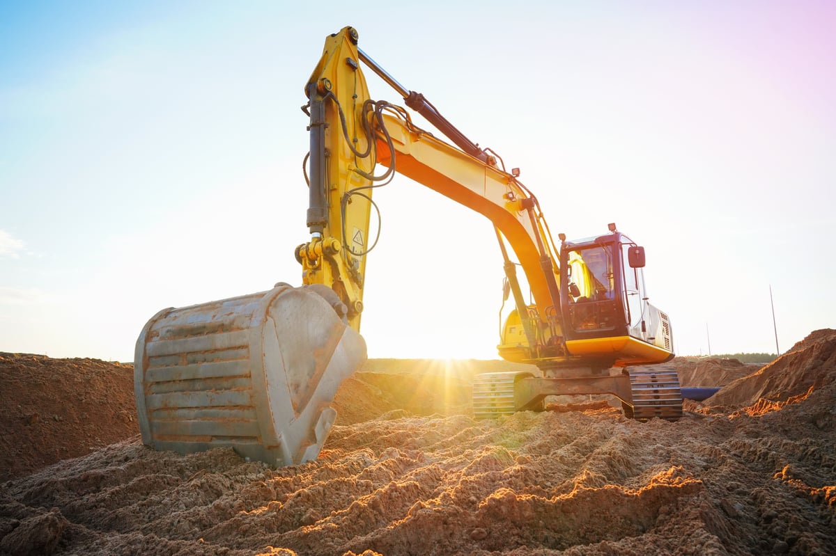 Excavator at construction site moving soil for sewage and trench construction at sunset