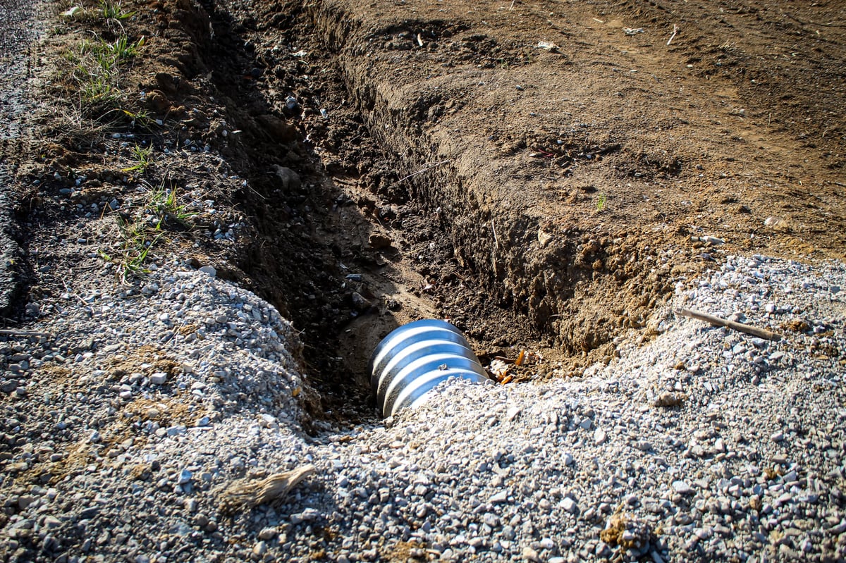 A culvert pipe installed in an excavated ditch area near construction as drainage design element