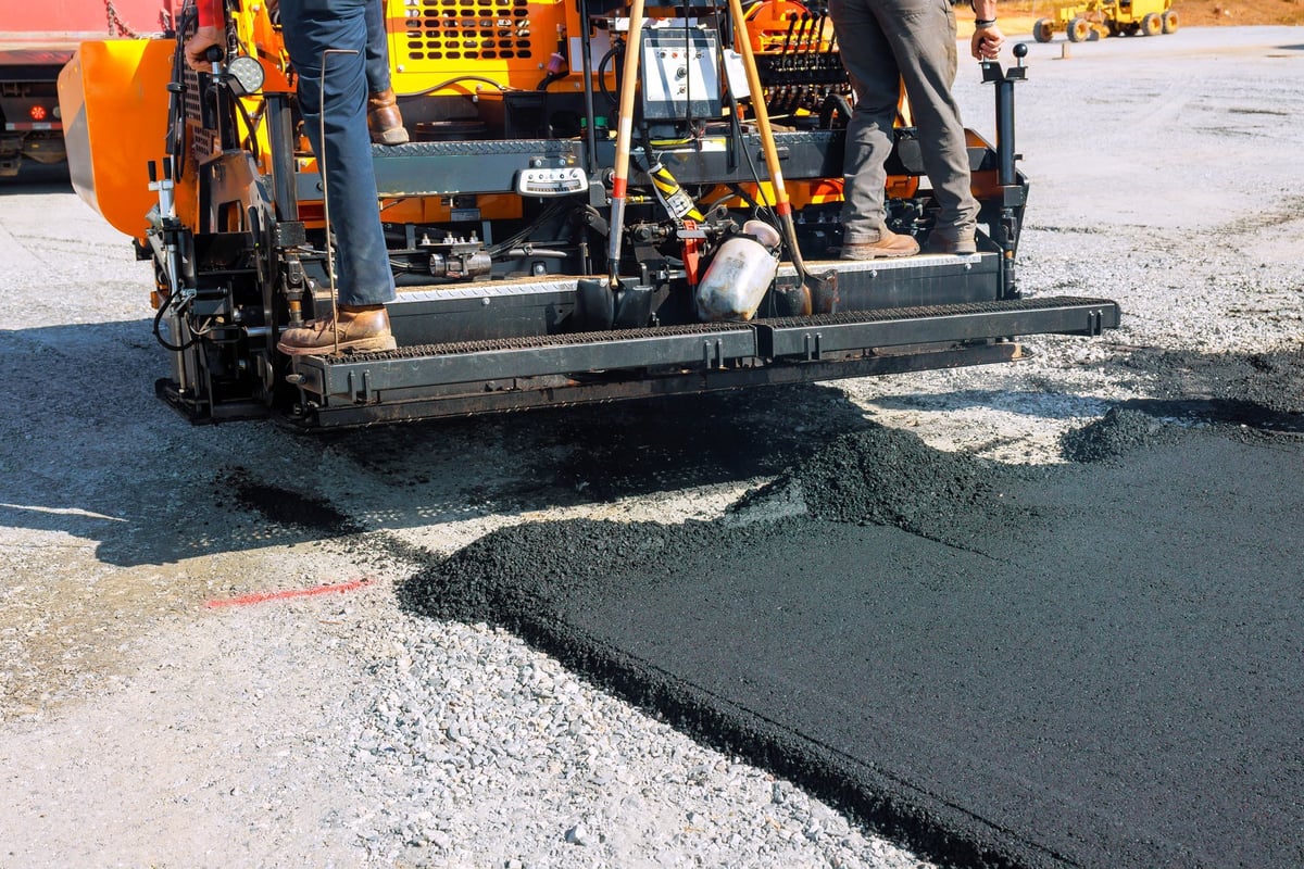 Workers operating a paving machine to lay new asphalt on a construction road site