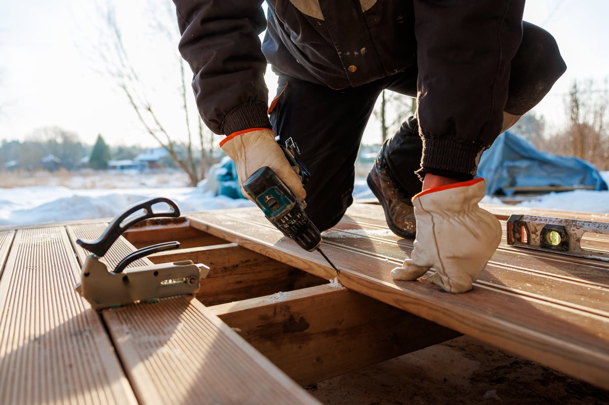 Tradesperson driving screws into composite decking while kneeling on timber joists