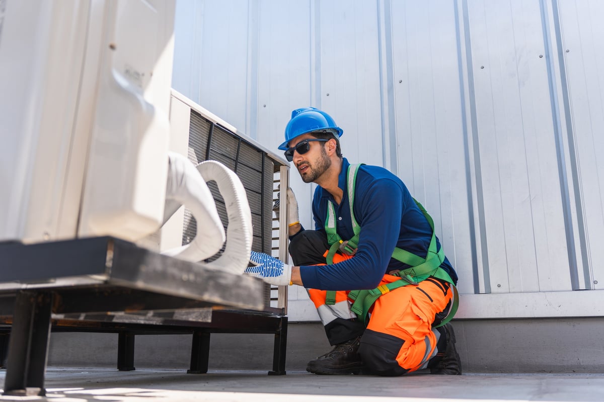 HVAC technician inspecting an outdoor air conditioning unit on a rooftop in safety gear
