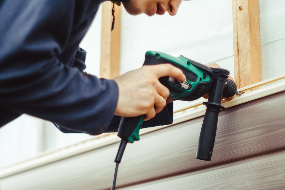 Worker installing beige siding panels on the facade of a house